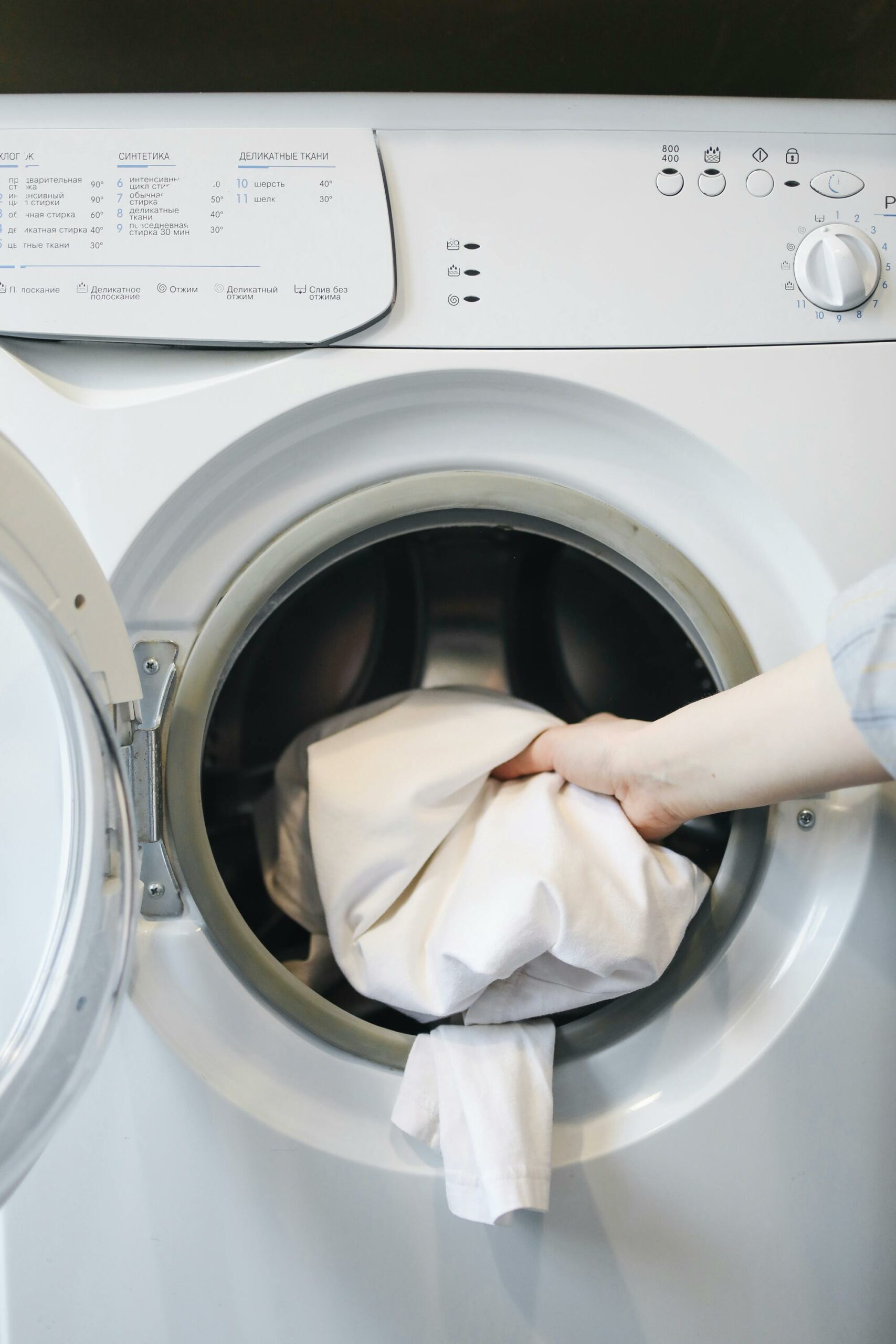 hand putting white sheet inside laundry washing machine